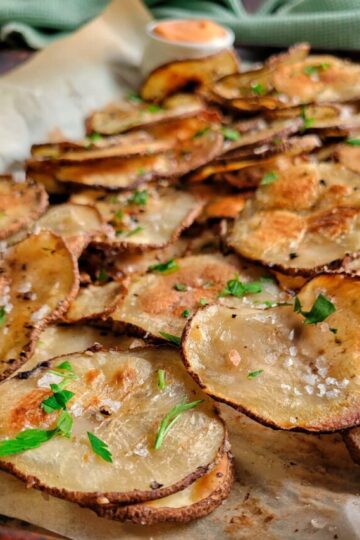 crispy thin slices of potatoes garnished with fresh chopped parsley, salt and pepper on a sheet pan
