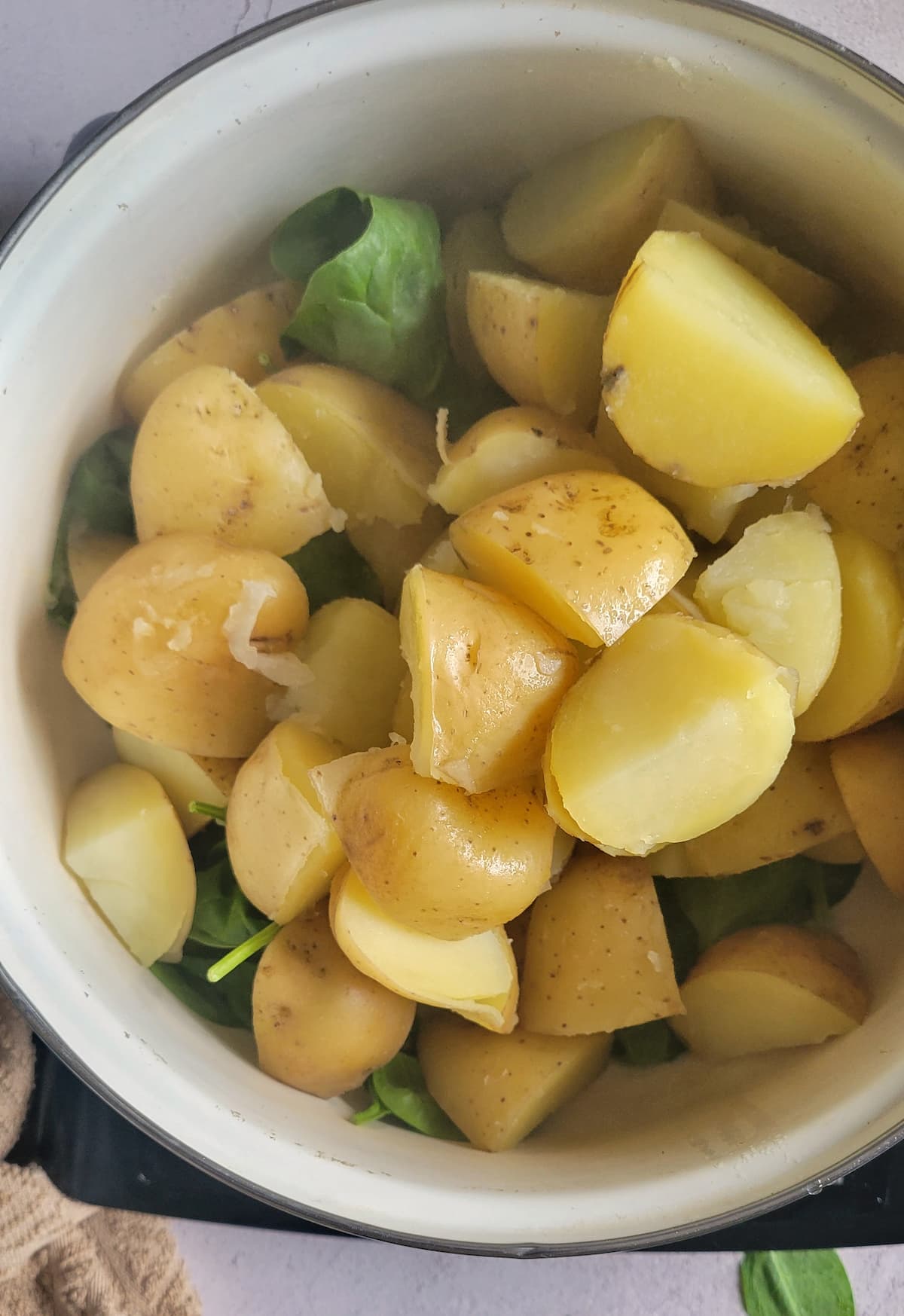 cooked cubed potatoes over a bed of raw spinach in a pot