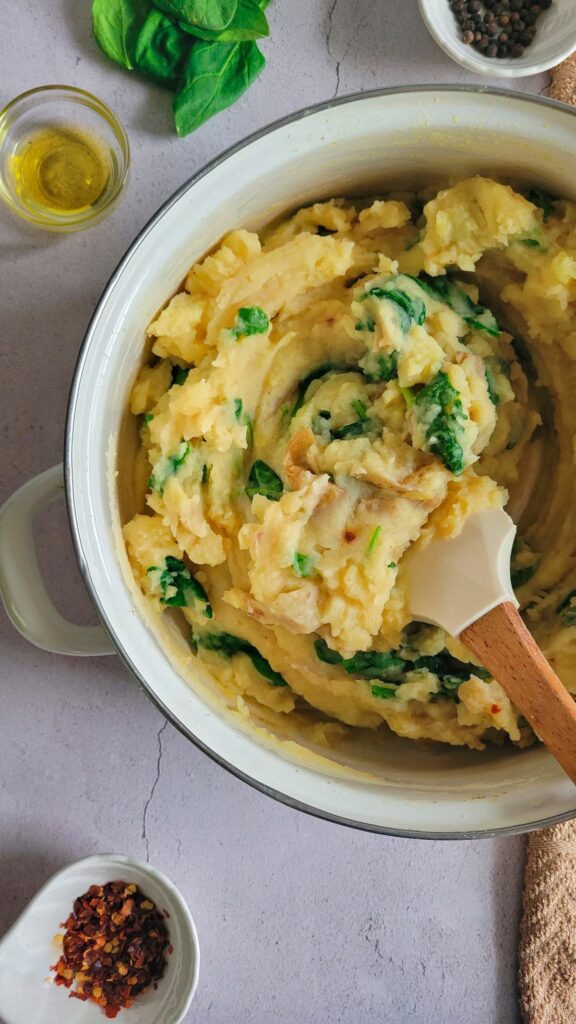 spinach mashed potatoes in a pot with a rubber spatula, spices and oil in the background
