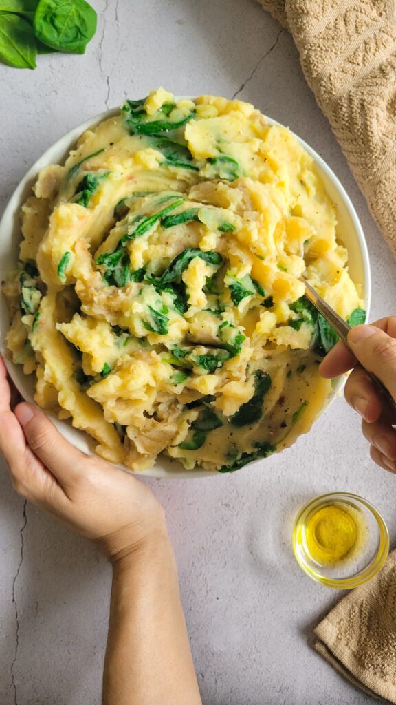 hand with a spoon holding a bowl of spinach mashed potatoes