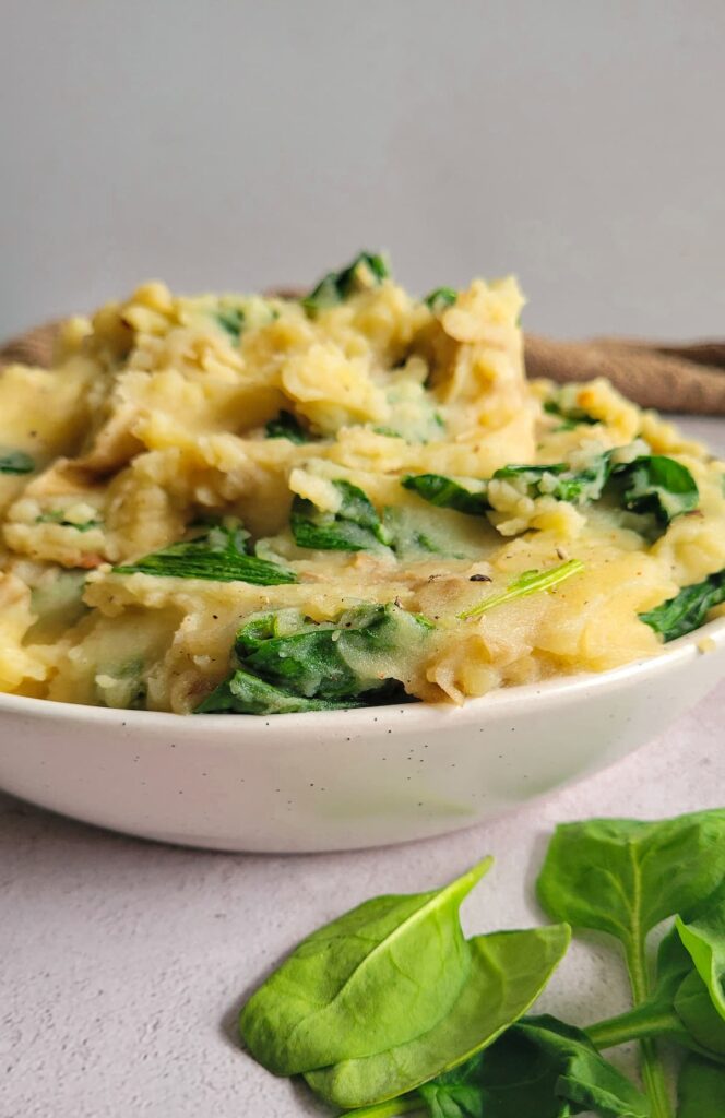 side view of a bowl of mashed potatoes with spinach, more spinach in the front