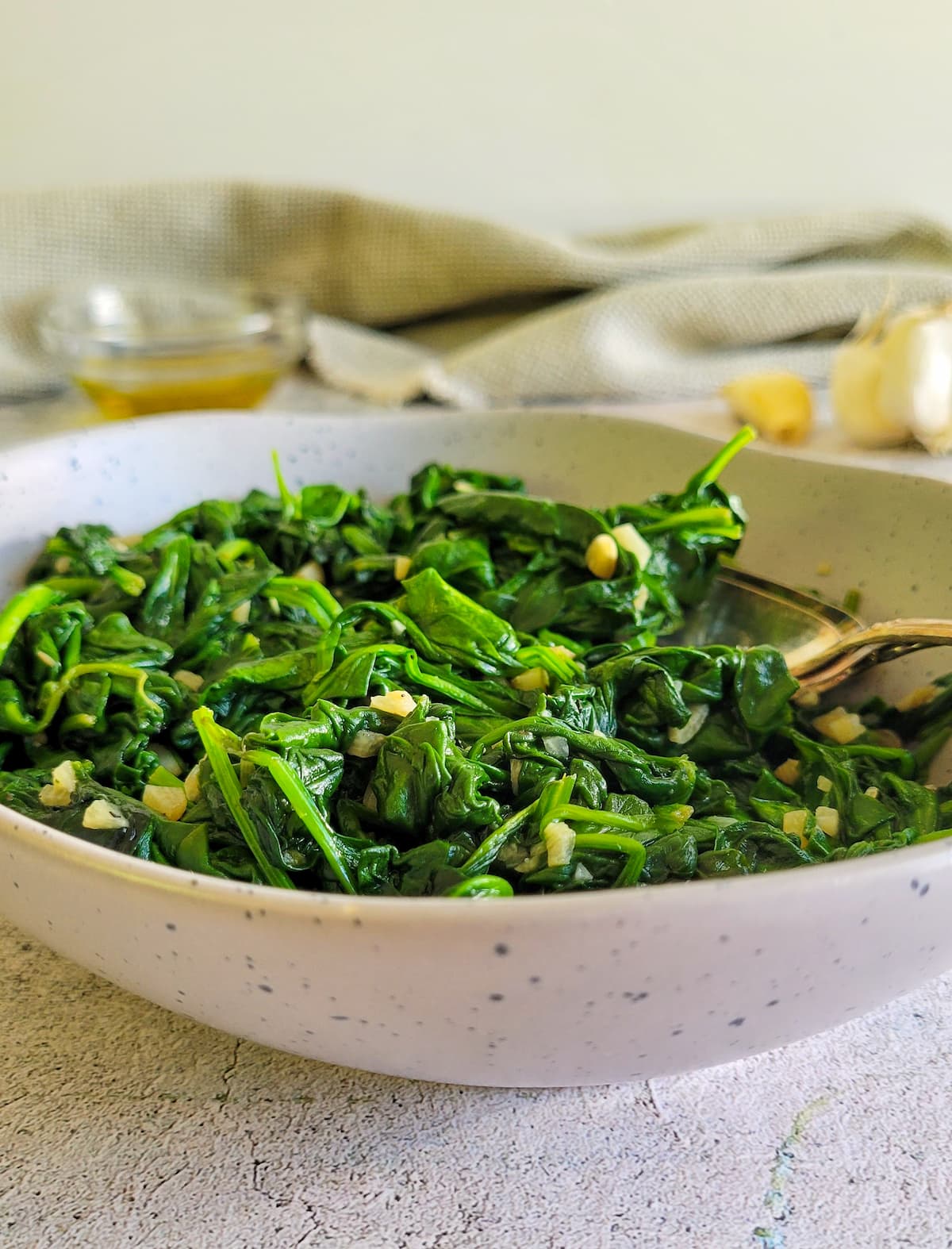 sauteed spinach and garlic in a bowl, olive oil and whole garlic cloves in the background