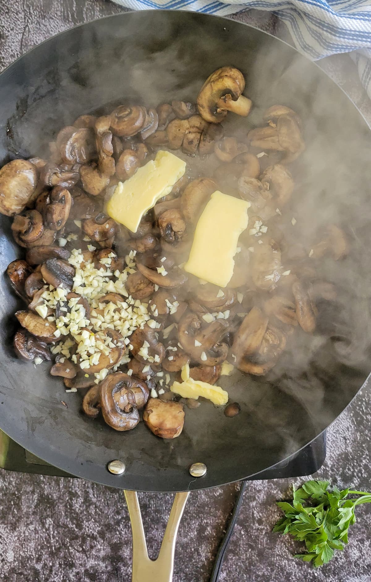 sliced mushrooms cooking in a skillet with minced garlic and butter