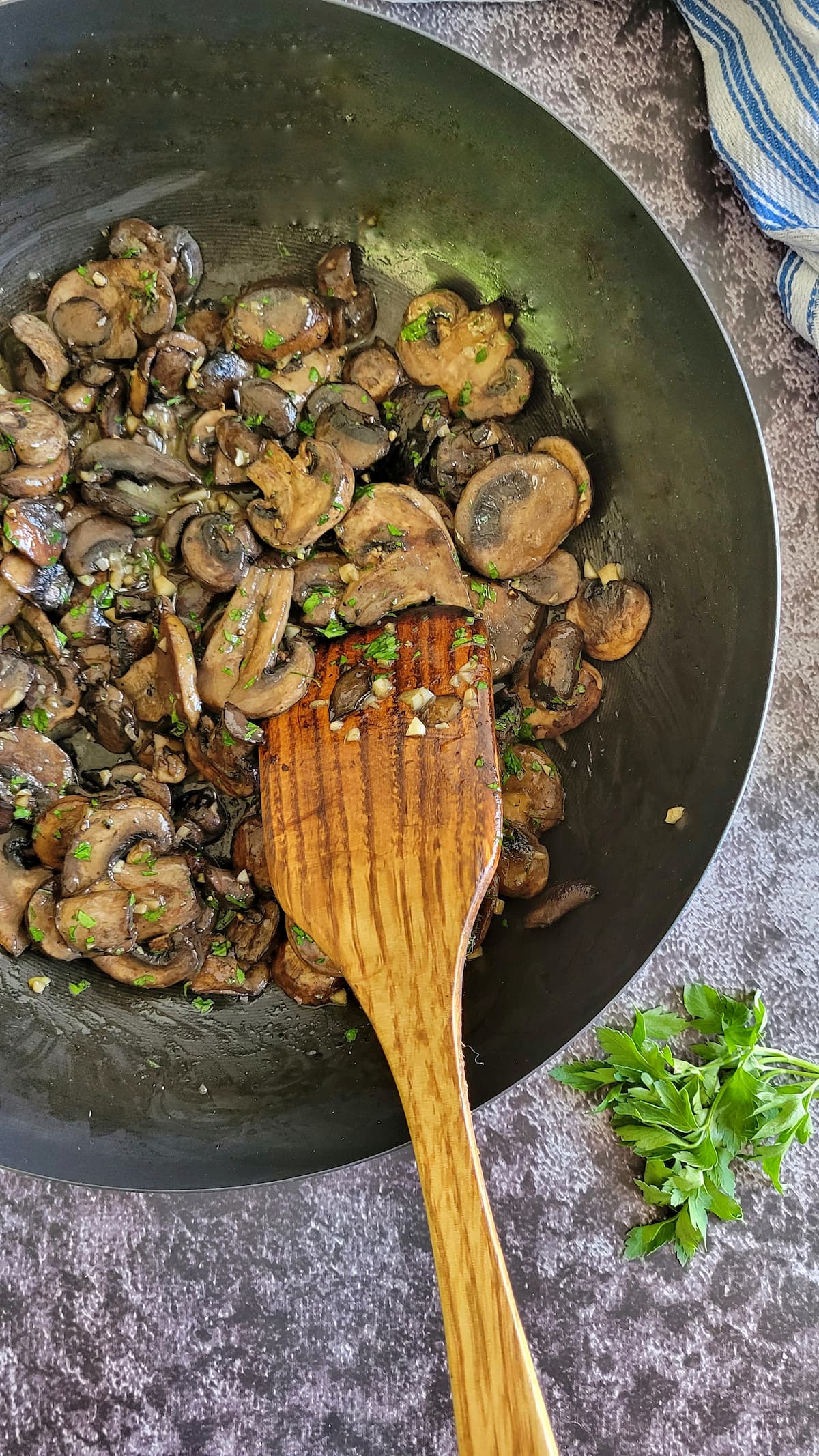 sliced cooked mushrooms, minced garlic and fresh chopped parsley in a skillet with a wooden spatula