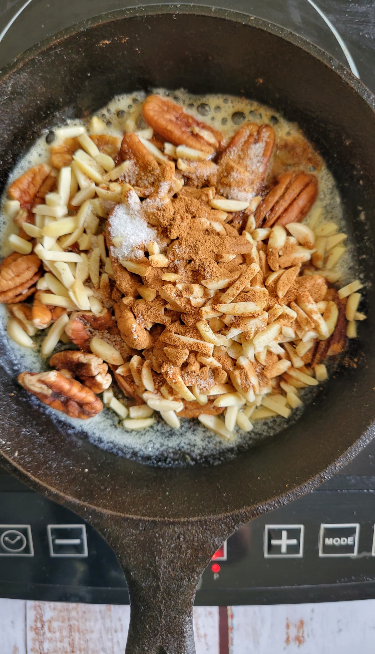pecans and slivered almonds in a cast iron skillet on a burner with spices and melted butter