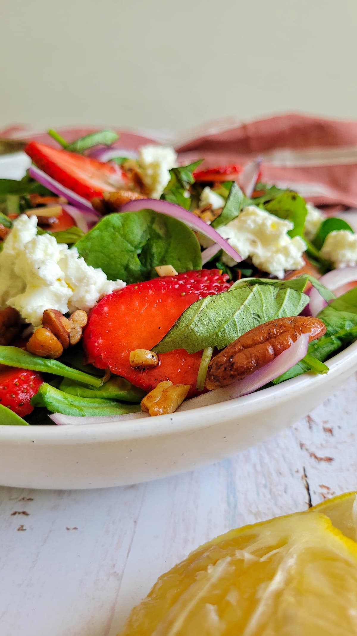 side view of a spinach salad with strawberries, goat cheese, red onions and pecans