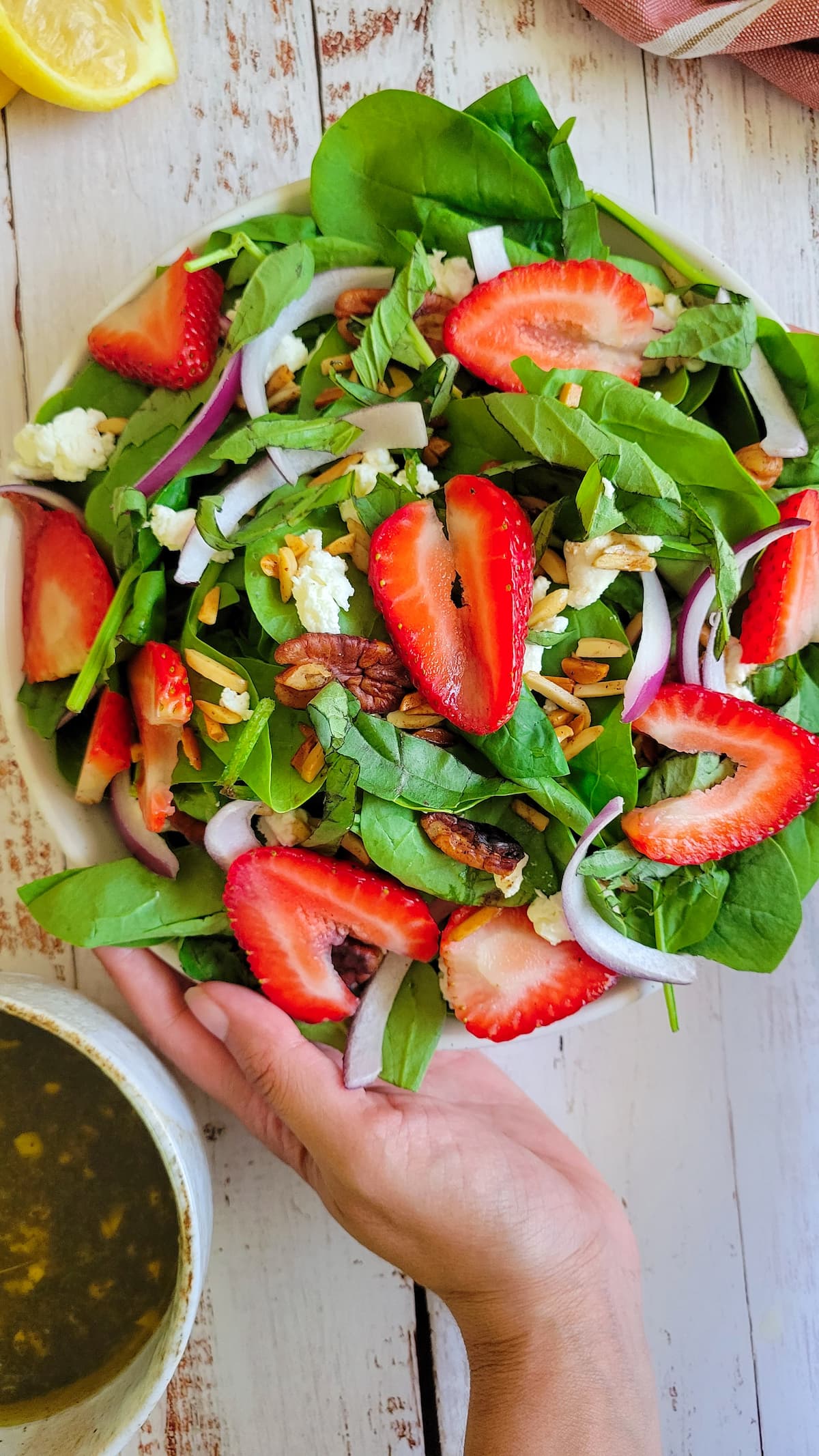 hand holding a bowl of spinach salad with strawberries, nuts, onions and goat cheese