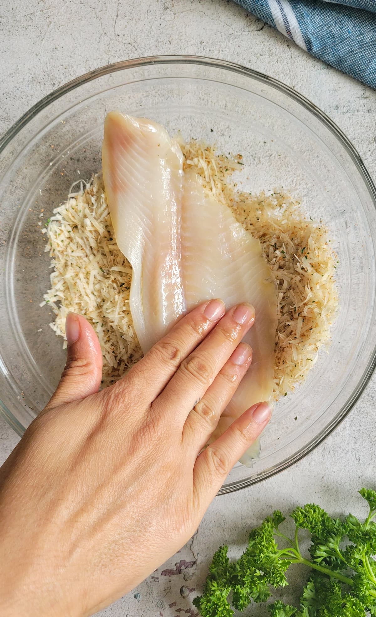 hand pressing a raw piece of white fish into a bowl of parmesan cheese and spices