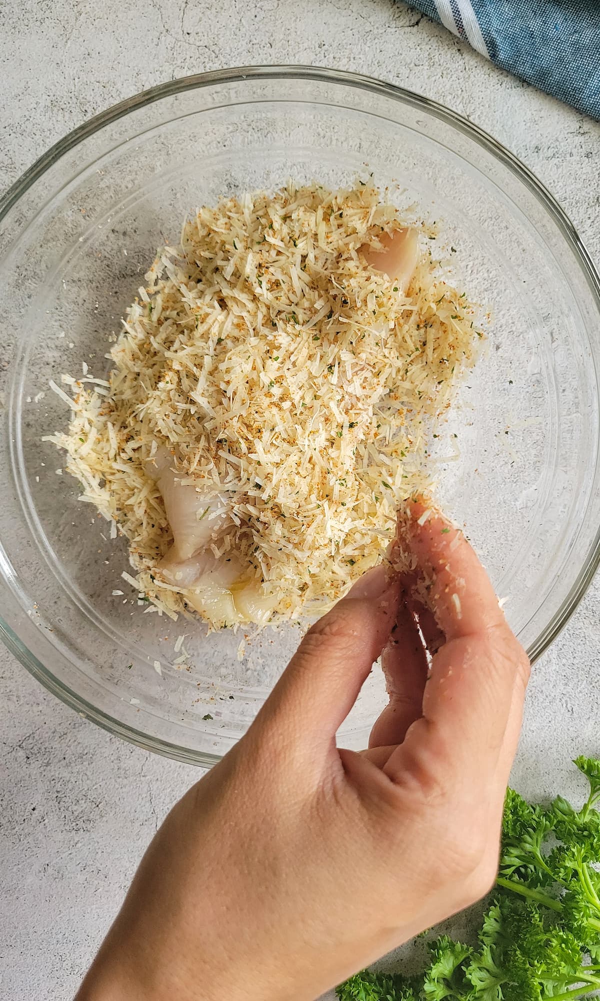 hand coating a fish fillet in a bowl of parmesan cheese and spices