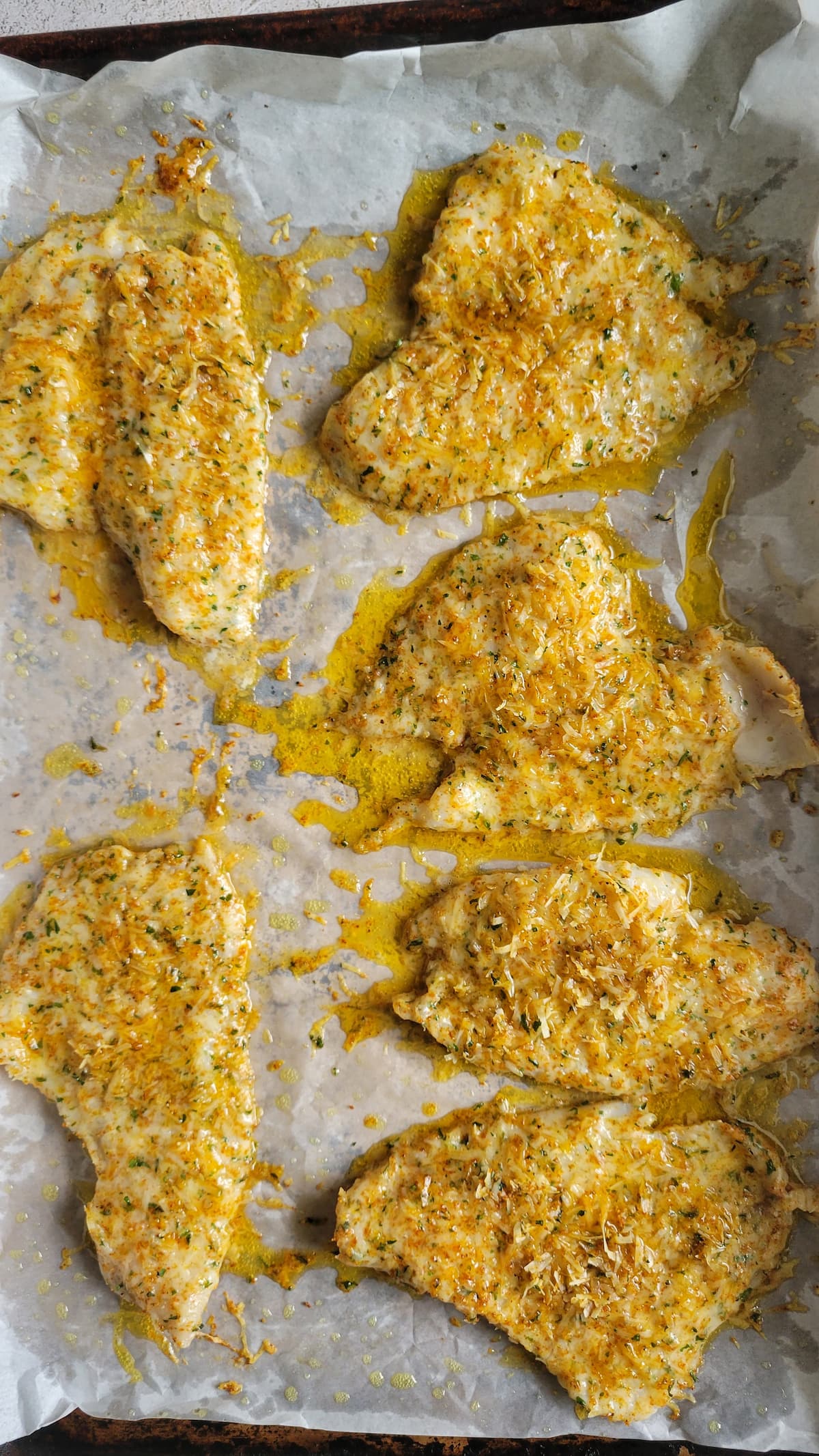 6 cooked parmesan crusted fish fillets on a parchment lined baking sheet