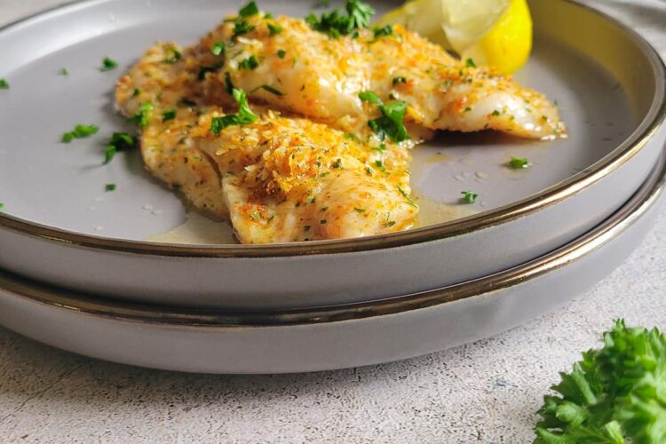 two crusted parmesan fish pieces on a double plate, garnished with fresh chopped parsley and a lemon wedge