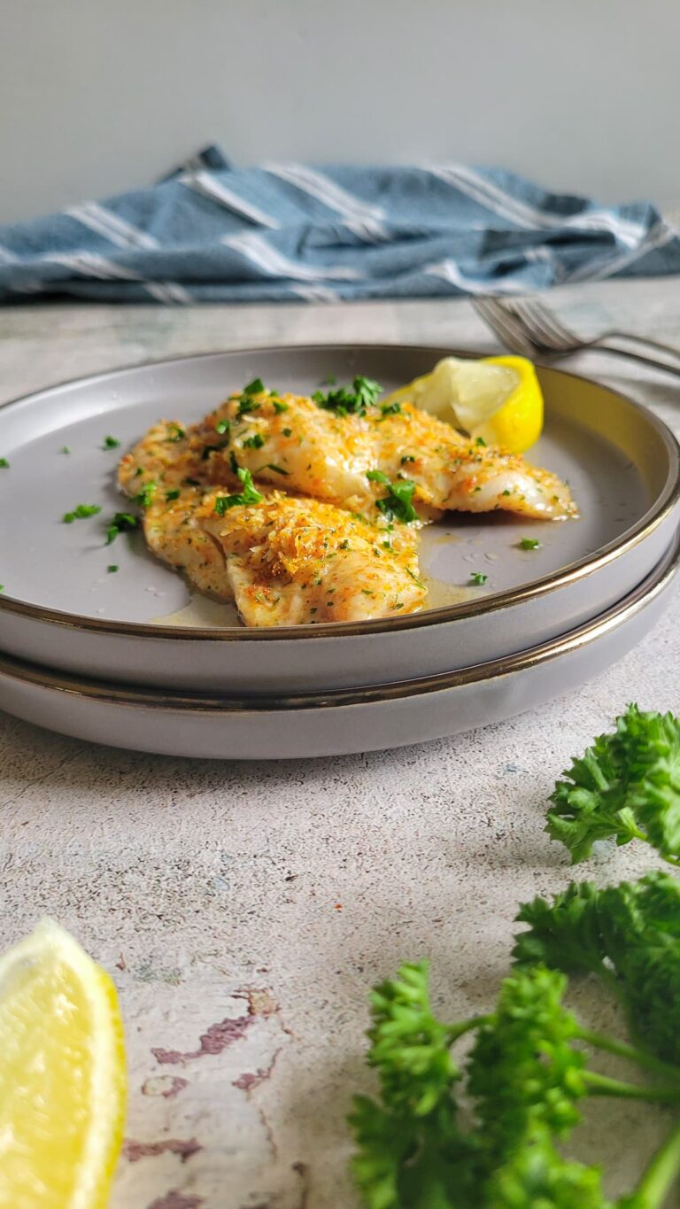 two crusted parmesan fish pieces on a double plate, garnished with fresh chopped parsley and a lemon wedge
