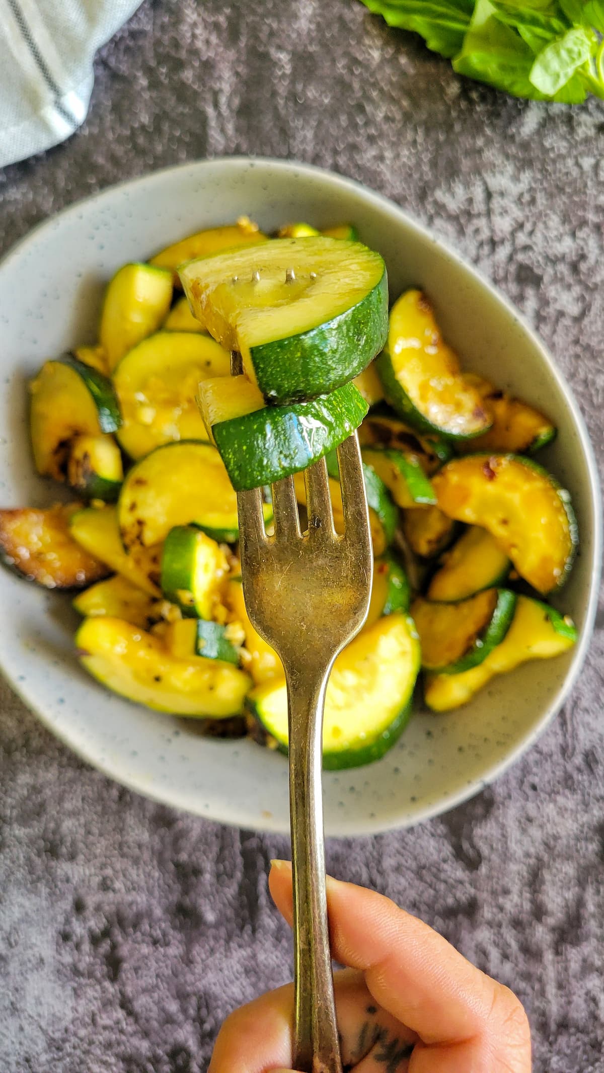 hand with a fork piercing two pieces of sauteed zucchini over a bowl of the rest of it