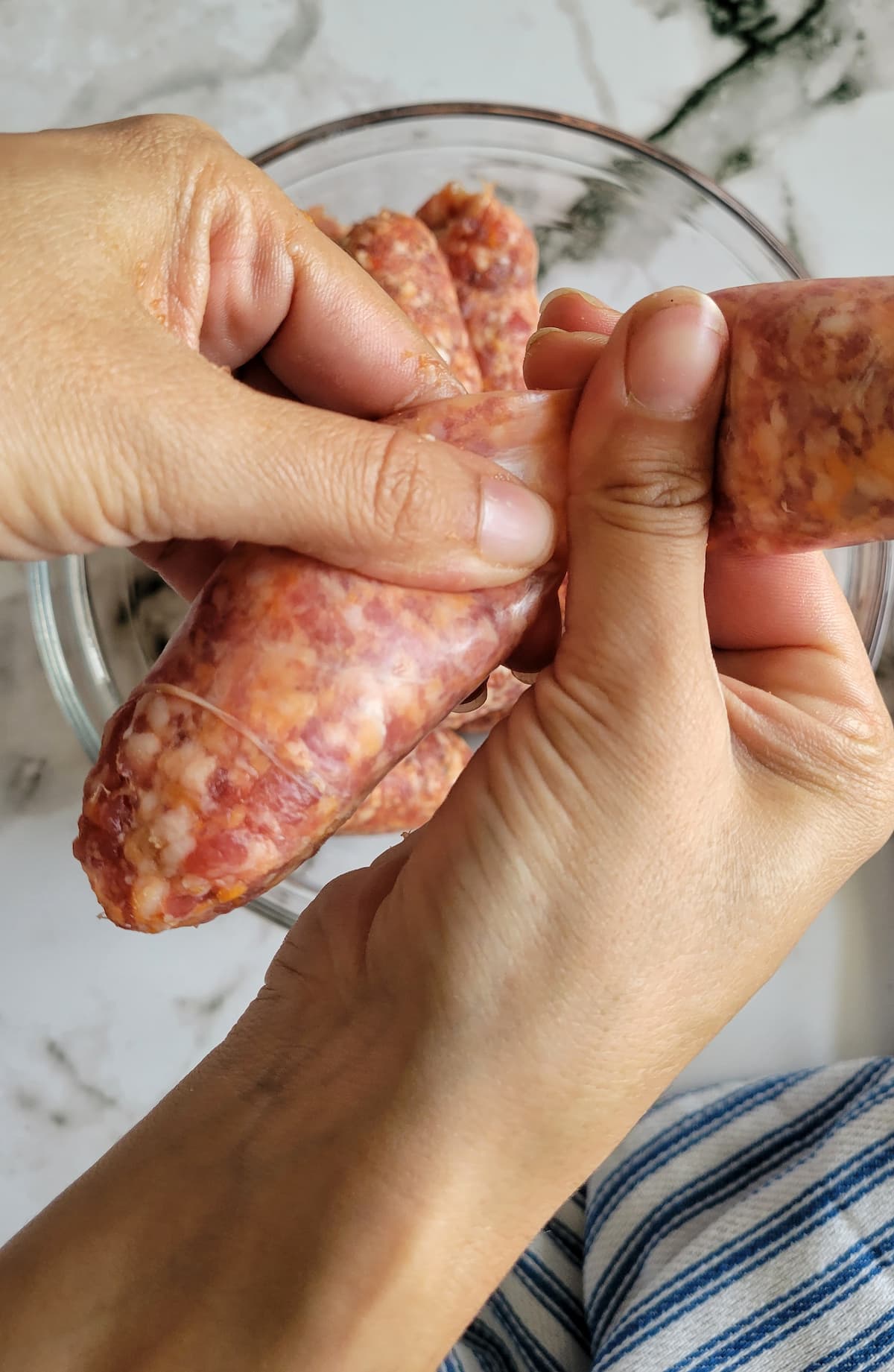 hands pushing sausage meat out of its casing