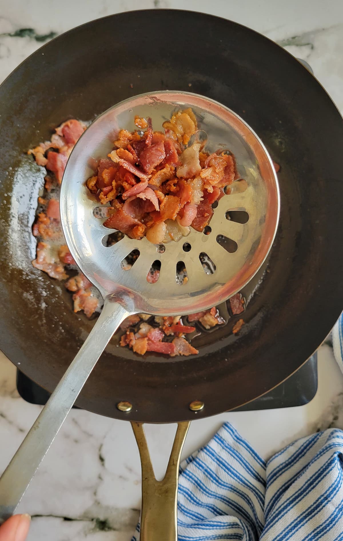 cooked crumbled bacon in a slotted spoon over a skillet with the rest