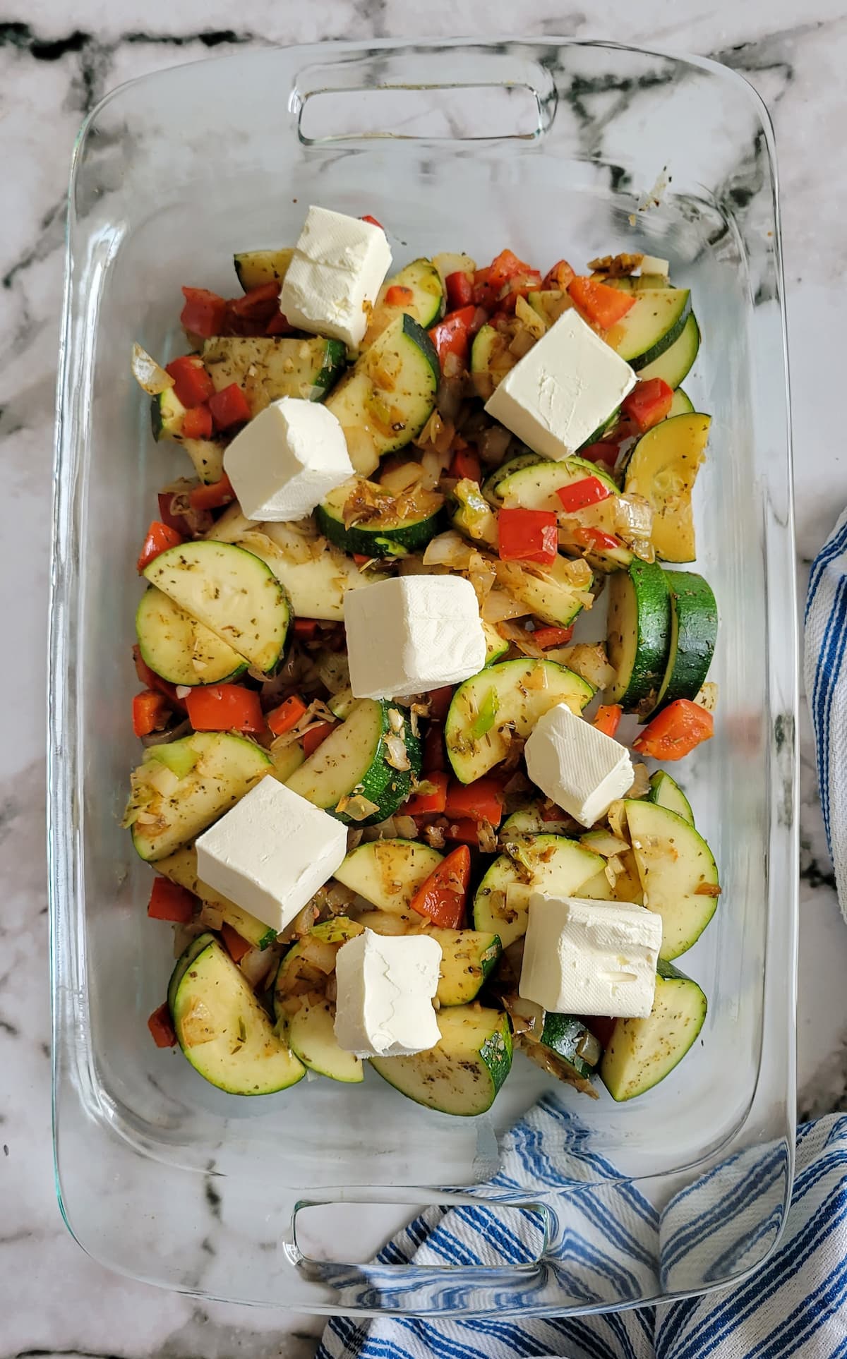 cooked zucchini, red peppers and onions in a casserole dish with cubed cream cheese