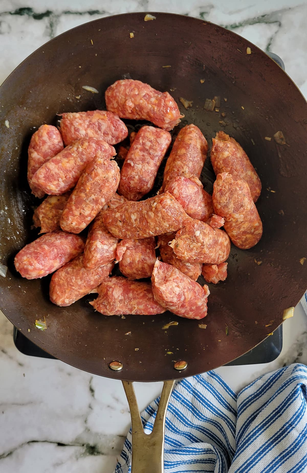 halved italian sausages out of their casing in a skillet