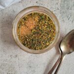 dry seasoning for chicken in a small glass jar beside two spoons.
