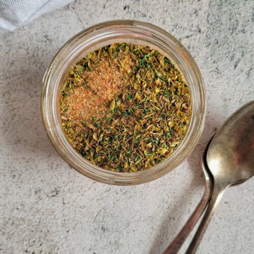 dry seasoning for chicken in a small glass jar beside two spoons.