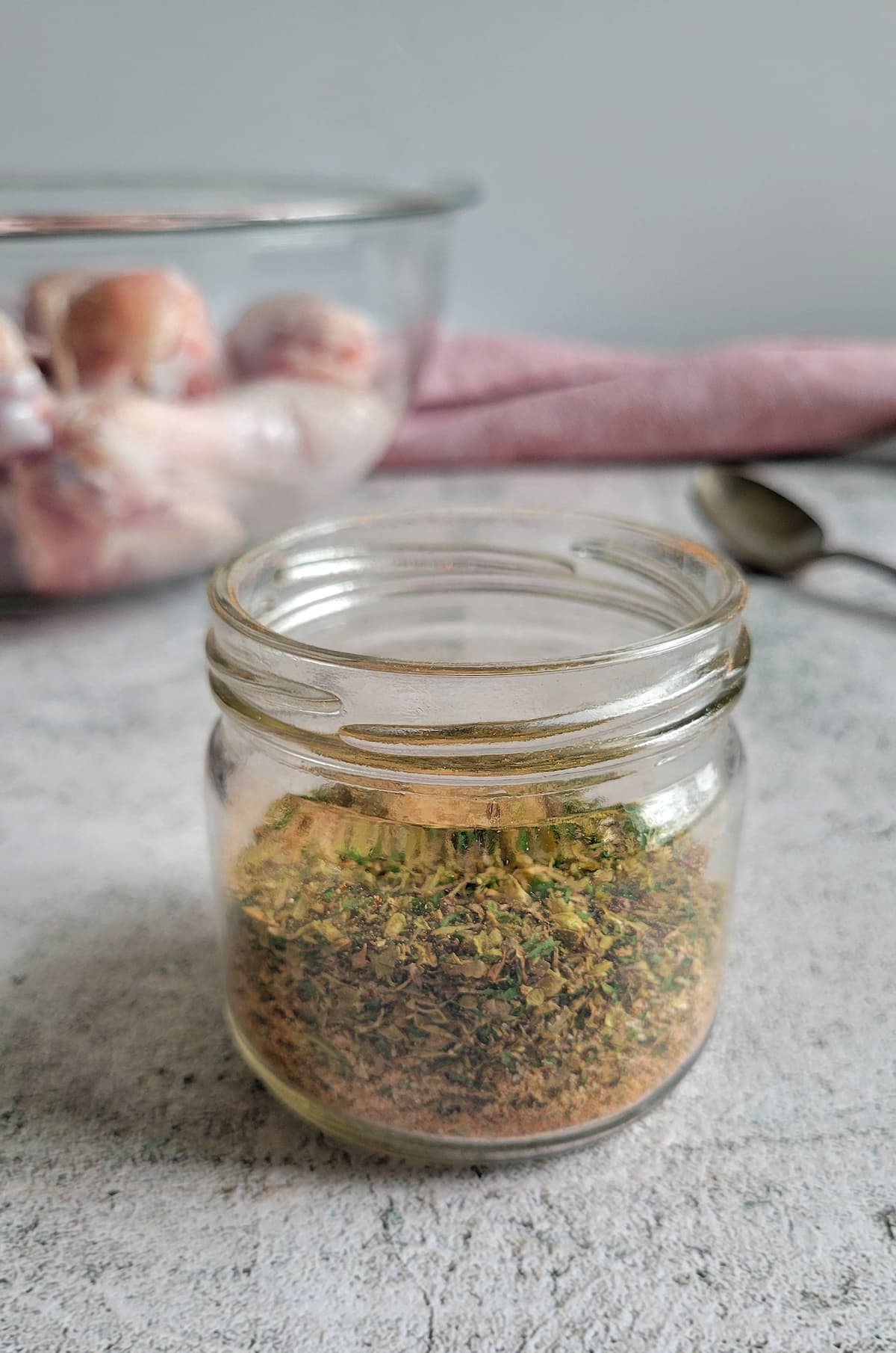 jar of spices, bowl of raw chicken drumsticks in the background