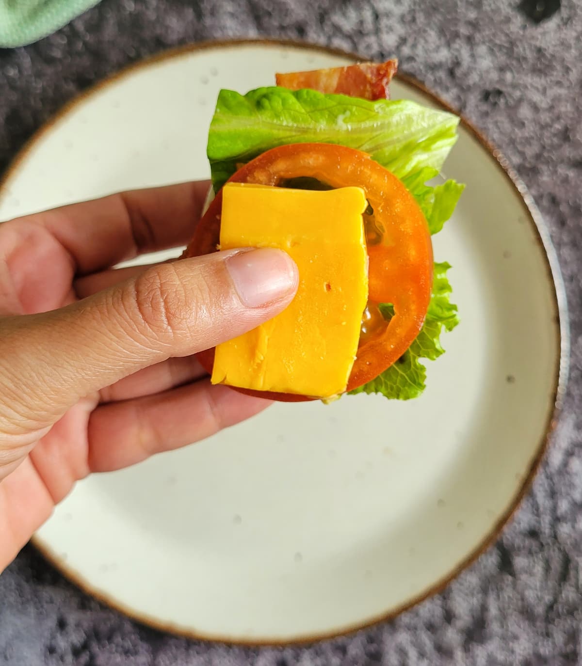 hand holding a piece of cheddar cheese on tomato with lettuce and bacon
