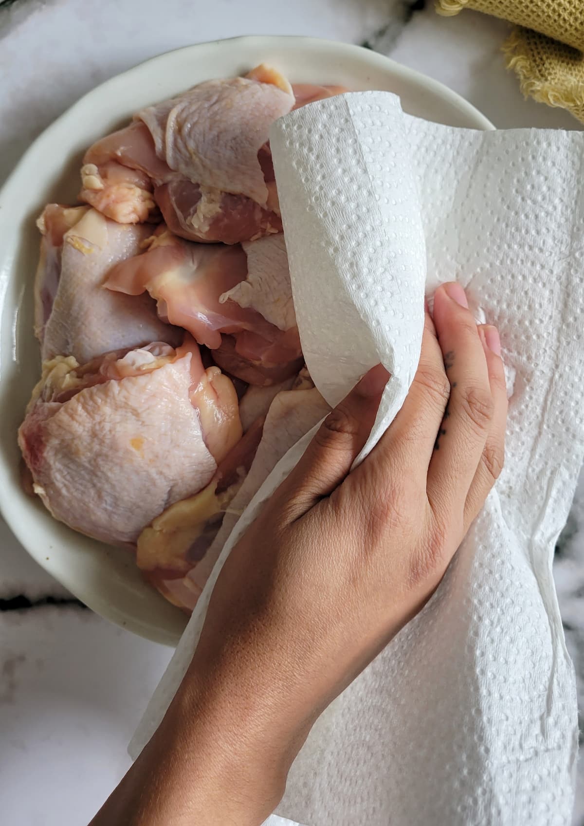 hand with a paper towel patting raw chicken thighs down