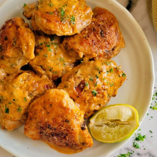 thai chicken with coconut cream sauce on a plate with a lime and fresh chopped cilantro