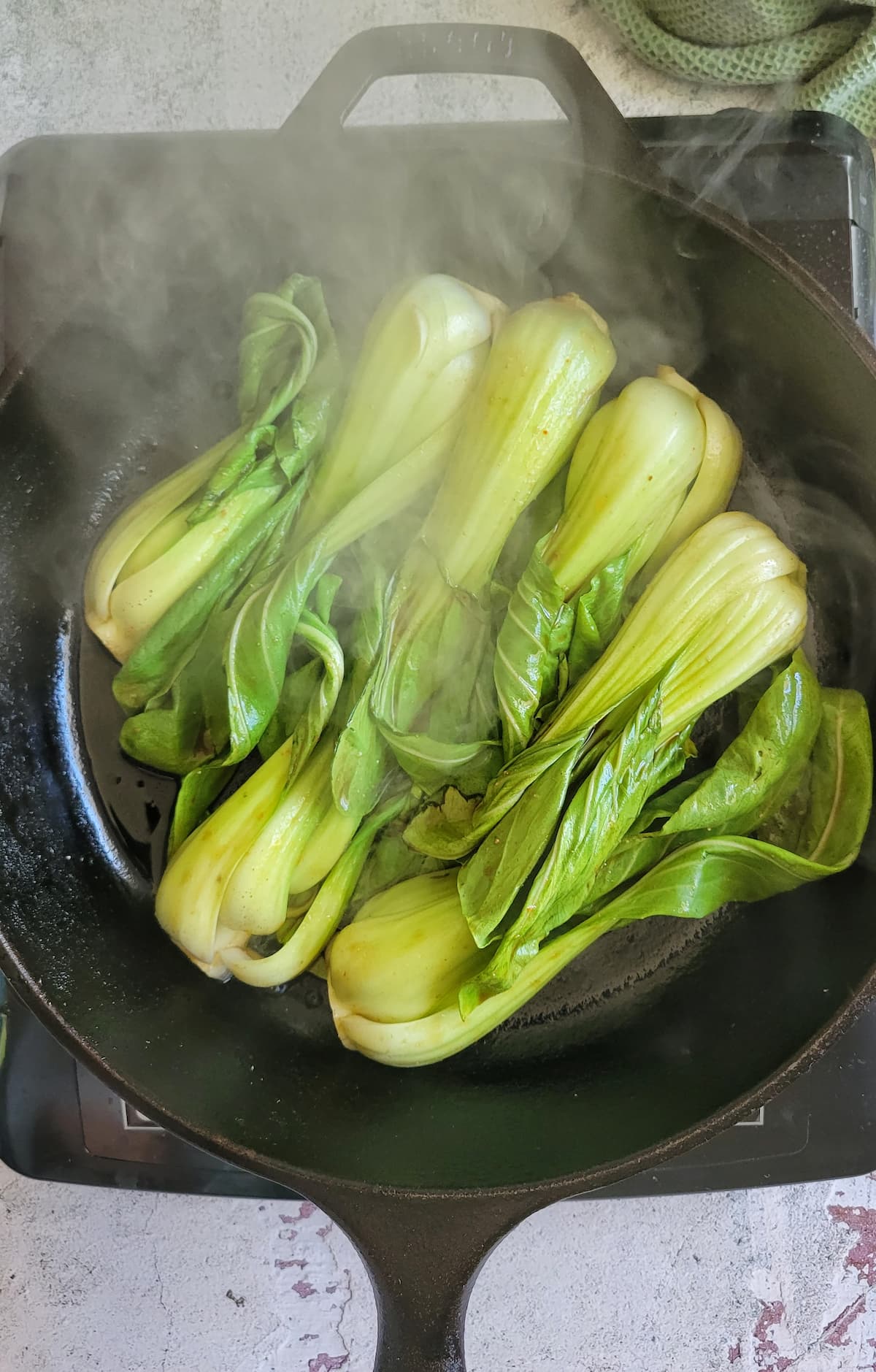 bok choy cooking in a cast iron skillet on a burner