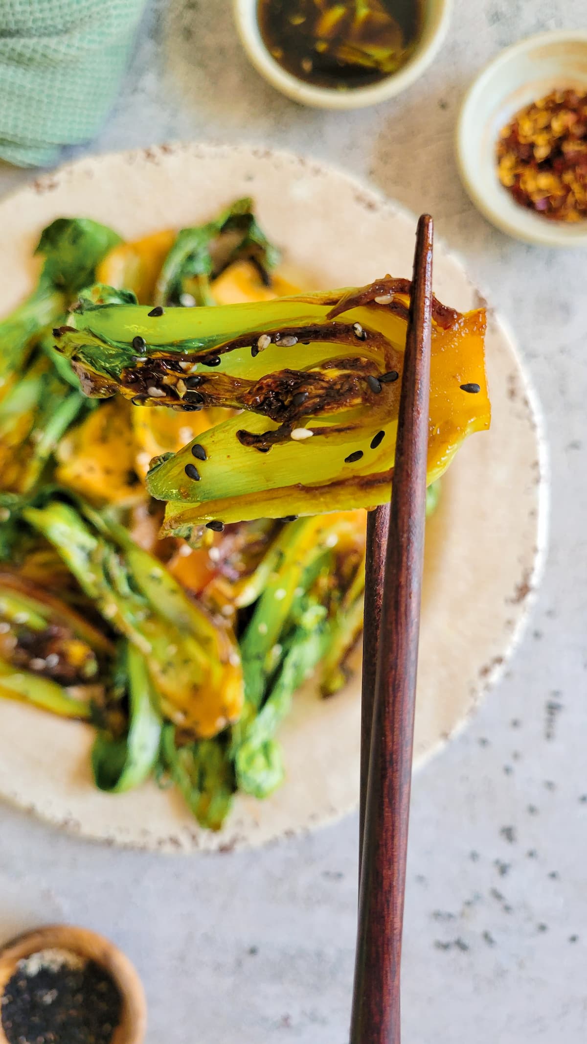 chopsticks holding a piece of caramelized bok choy with sesame seeds above a plate with the rest of it