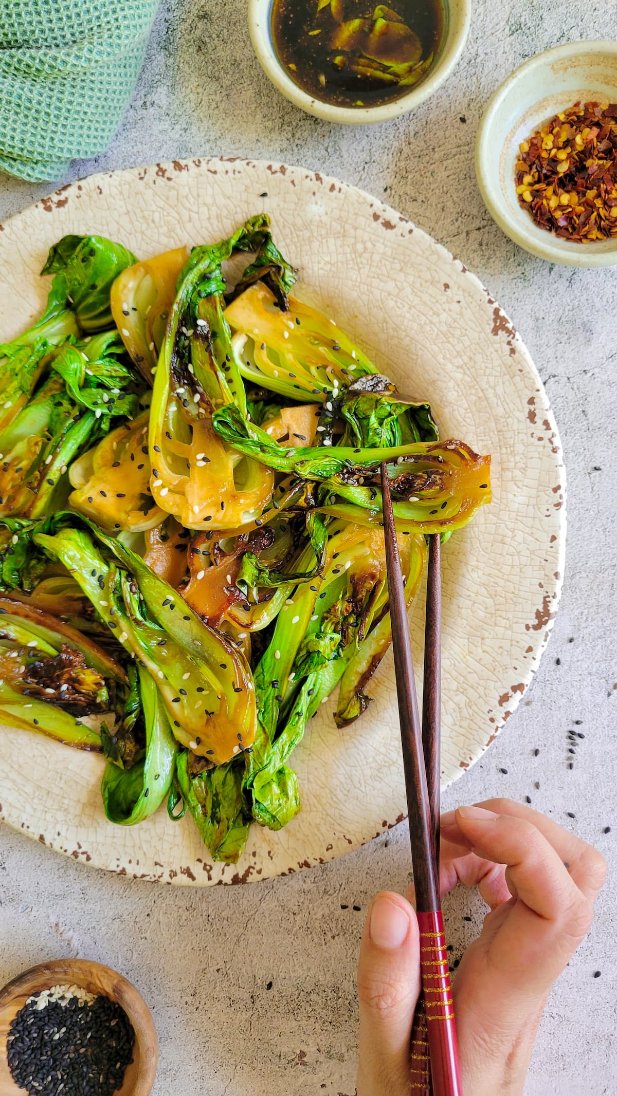 hand holding onto a piece of bok choy with chopsticks in a plate with more