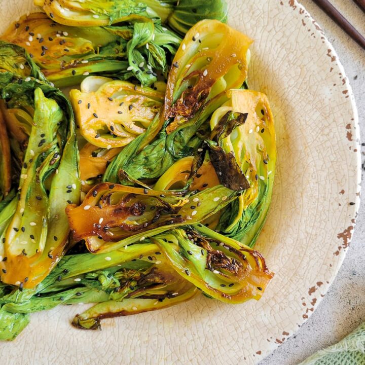 caramelized bok choy on a plate with sesame seeds, chopsticks in the background