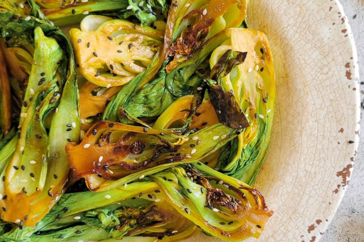 caramelized bok choy on a plate with sesame seeds, chopsticks in the background
