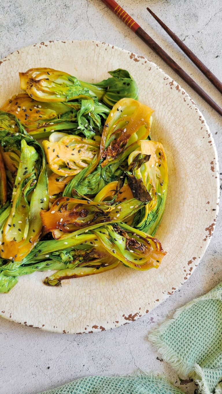 caramelized bok choy on a plate with sesame seeds, chopsticks in the background