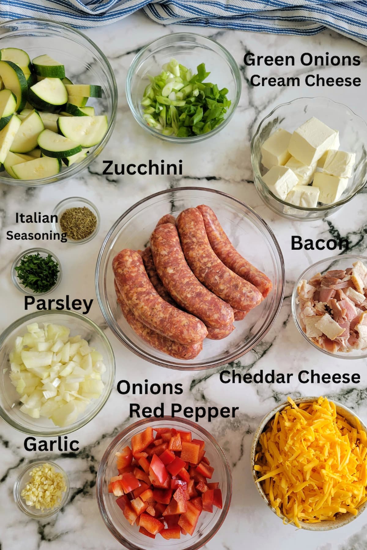 ingredients for sausage casserole with zucchini - zucchini, italian sausage, cheddar cheese, cream cheese, parsley, green onions, onions, red pepper, garlic, bacon, italian seasoning