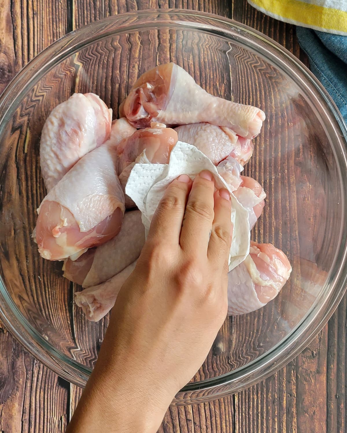 hand with a paper towel patting raw drumsticks dry in a bowl