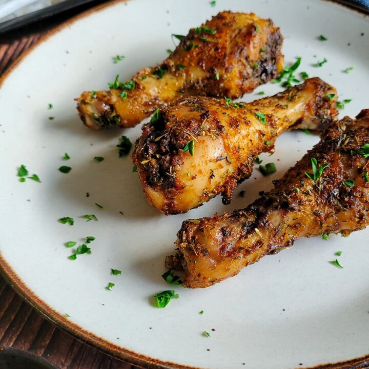 3 cooked drumsticks on a plate garnished with fresh chopped parsley, tray with more in the background