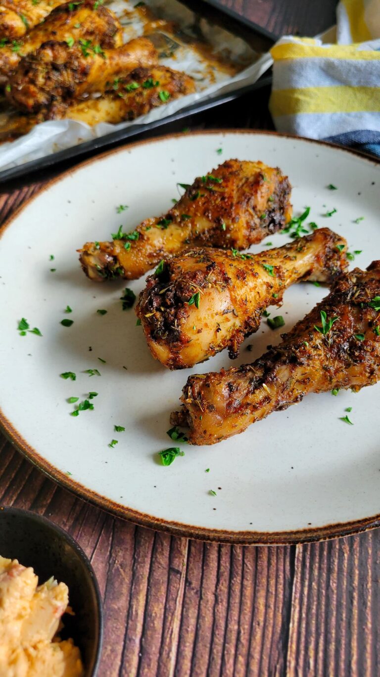 3 cooked drumsticks on a plate garnished with fresh chopped parsley, tray with more in the background