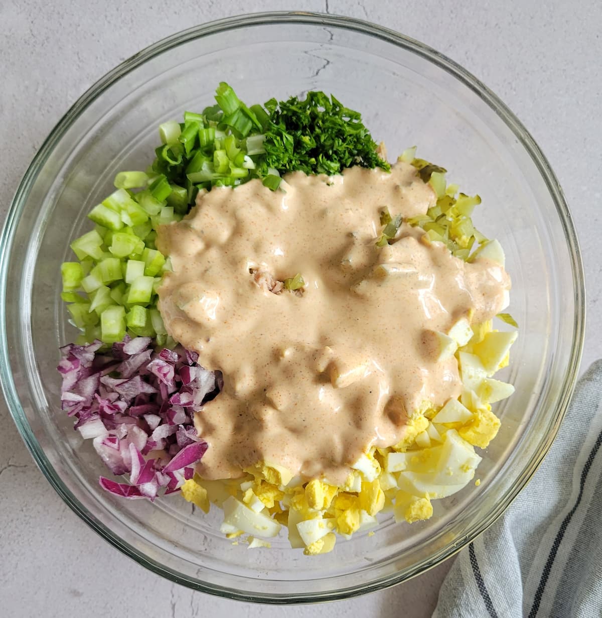 diced celery, red onion, green onion, parsley and chopped hard boiled eggs unmixed in a bowl topped with a creamy sauce