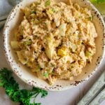tuna salad with eggs in a bowl, lettuce in the background with serving spoons