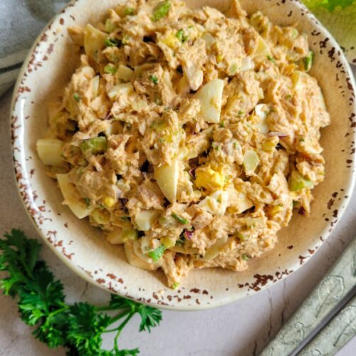 tuna salad with eggs in a bowl, lettuce in the background with serving spoons