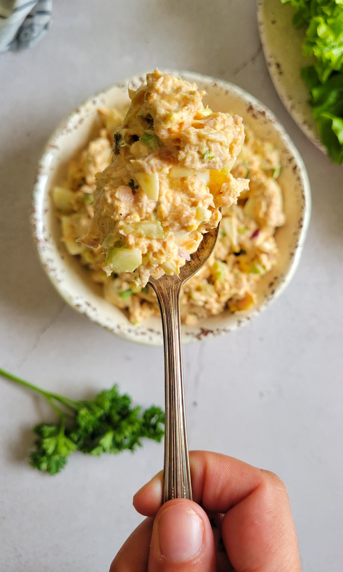 hand holding a spoonful of tuna salad with egg over a bowl with the rest of it