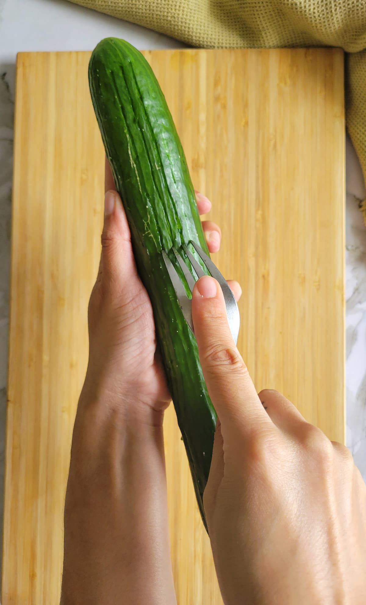 hand with a fork scraping an unpeeled cucumber over a cutting board