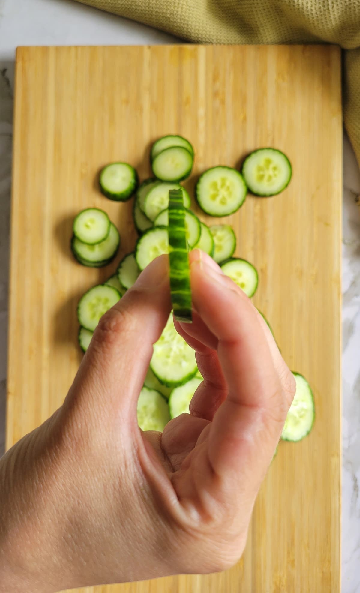hand holding a thin slice of cucumber over a cutting board with the rest of them