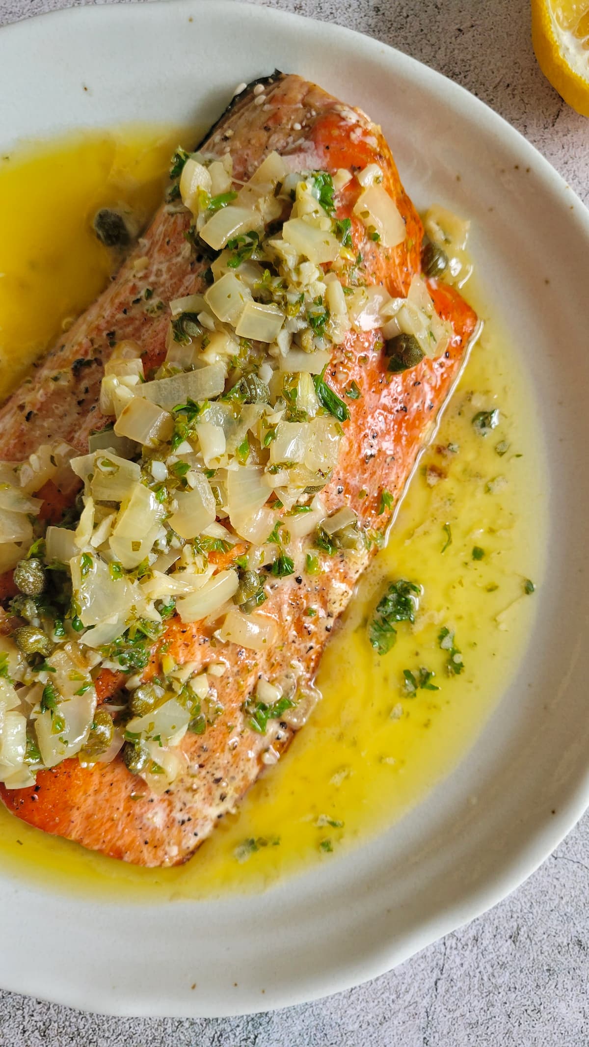 pan seared salmon on a plate with lemon caper butter sauce, chopped cooked white onions on the salmon