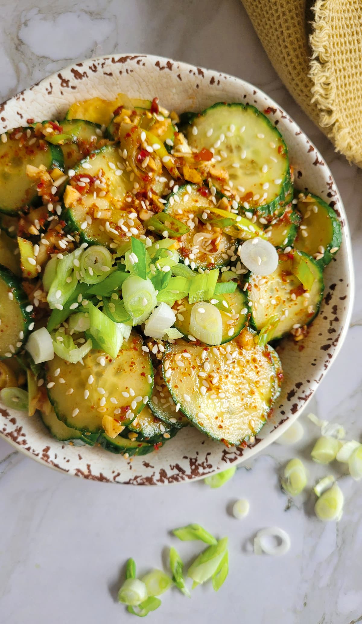 a bowl of cucumbers in a spicy sauce with sesame seeds and green onions