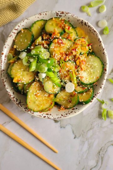 bowl of cucumbers with green onions, sesame seeds and a spicy sauce