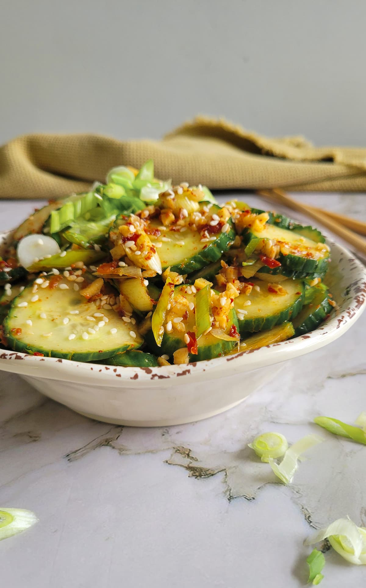 side view of a bowl of cucumbers in a spicy sauce with sesame seeds and green onions