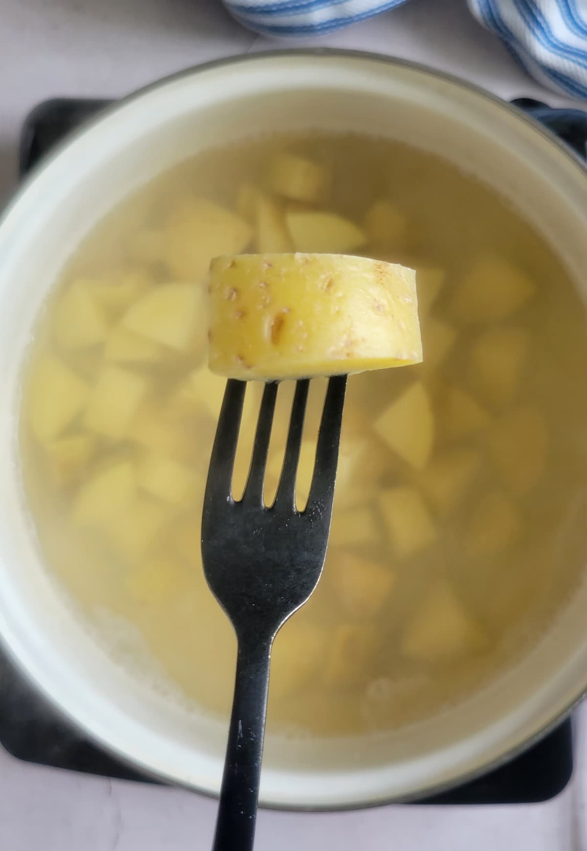 hand piercing a chunk of potato over a pot of the rest in water