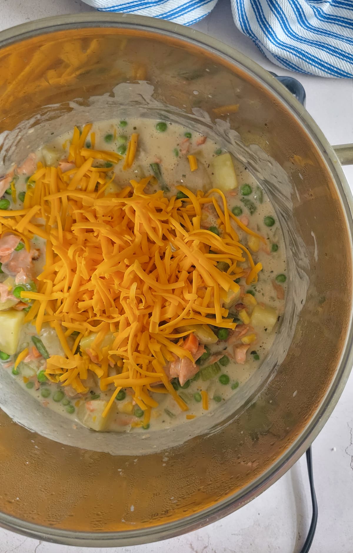 grated cheddar cheese in a pot with salmon, cream and potatoes