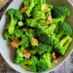 garlic broccoli in a bowl, unpeeled garlic cloves on the side